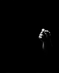 Fototapeta premium Clenched fist emerges from darkness, symbolizing strength and determination. contrast highlights hand texture and form
