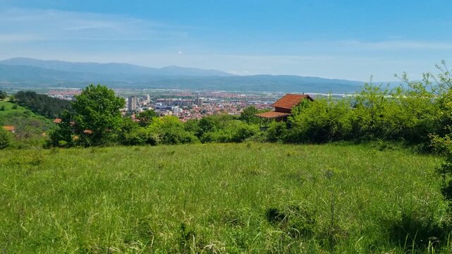 Panoramic view over the rolling hills of southern Serbia, with the rooftops of Leskovac visible on the horizon beneath a clear blue sky on a sunny spring day