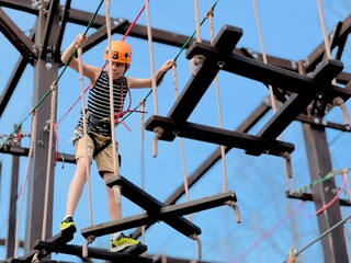 a teenage boy in outdoor rope park passing obstacle course.