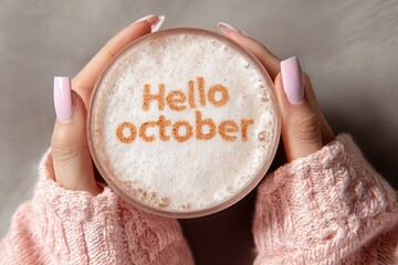 woman hands in pink knit sweater holding cup of coffee with crema. Text Hello october on it. 
