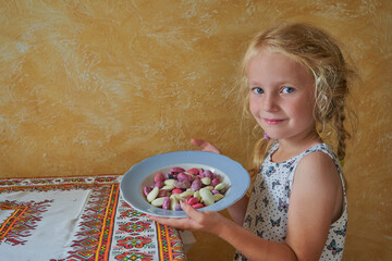 little girl holding a bowl of beans, little girl with pigtails holding a plate of peeled red and white beans