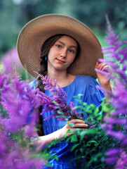 Close up portrait of girl wearing a straw hat holds lavender in her hands, smiling softly as she stands in a lavender field bathed