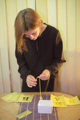Woman meticulously assembling a yellow paper banner for a celebration, threading a string through...