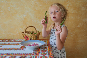 little girl holding bean pods, child standing at the table holding bean pods, peeling beans in the kitchen