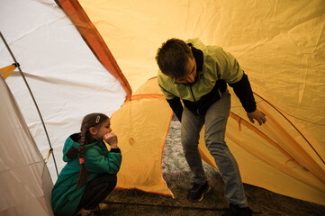 Father and daughter bonding while setting up a yellow tent during a camping adventure in the...