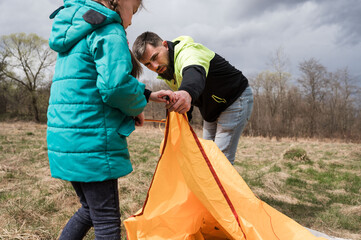 Family camping adventure unfolds as a father and daughter set up an orange tent under a moody sky...