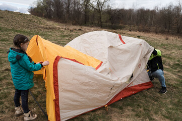 Children explore outdoor adventures while setting up a colorful tent in a tranquil field under a...