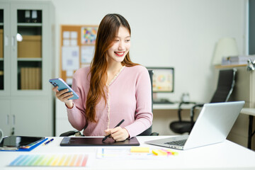 Asian designer using digital pen and laptop in a creative office, showcasing professional work,...