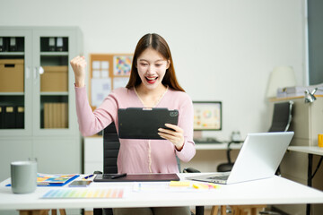 Joyful designer celebrates achievement while using tablet in modern workspace, showcasing...