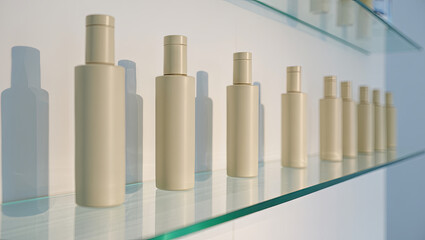 A row of beige cosmetic containers is neatly arranged on a glass shelf in a contemporary beauty store. The soft daylight enhances their clean and elegant design