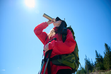 Woman in hiking gear taking a sip of water during mountain hike. Sporty female standing in front of...