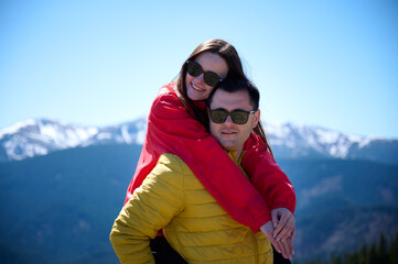 Happy couple enjoying mountain adventure. Man carrying smiling woman on his back. Outdoor romance,...