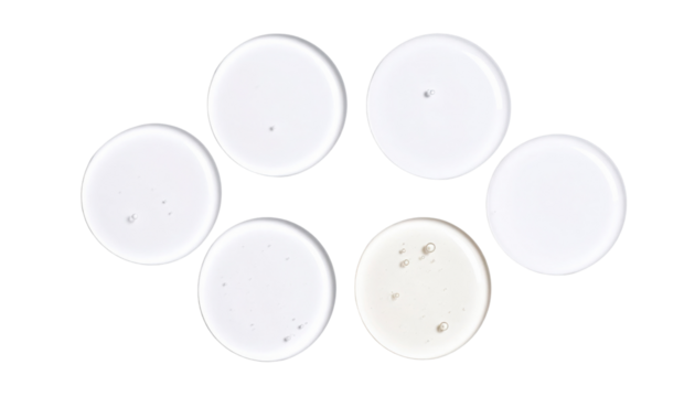 Six clear round liquid-filled petri dishes arranged with one slightly different in color, showing small air bubbles inside.