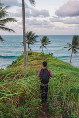 Hiker walking to sea edge on lush tropical cliff with palm trees and ocean waves. Perfect for adventure, hiking, and tropical retreat visuals.