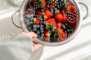 Fresh summer berries in a colander with soft sunlight and shadows.