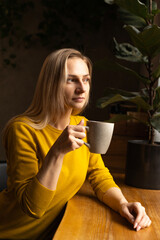 Woman drinks tea near a café window, enjoying a quiet afternoon alone.