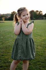 Child girl standing in green dress in the park during summer evening.