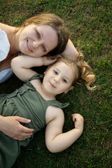 Smiling mother and daughter resting in the grass.