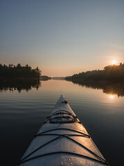 Front of kayak heading into still water of lake at sunrise in Canada.