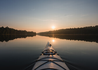 Front of kayak heading into still water of lake at sunrise in Canada.