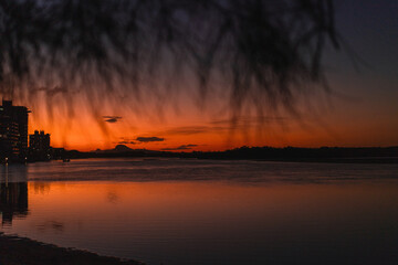Silhouette of city skyline at sunset with reflections on calm water