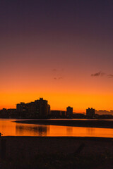 City skyline at sunset, reflections, vibrant orange and purple sky