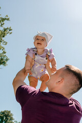 Father lifting baby girl against blue sky