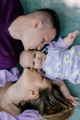 Parents kissing baby while lying on blanket