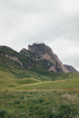 Dramatic mountain landscape in the Dolomites with grassy fields and clouds.