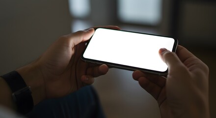 Close up of a person holding a mobile phone with a blank white screen in landscape orientation indoors.