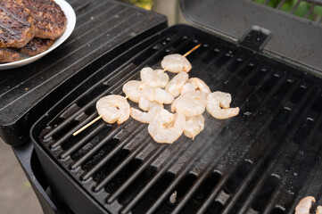 Grilling shrimp skewers on outdoor barbecue grill with juicy burgers