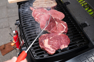Grilling juicy steaks on outdoor barbecue grill with smoke rising in backyard