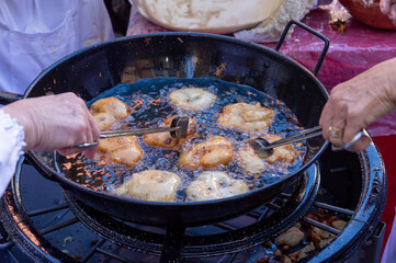 Two people are frying donuts in a pan
