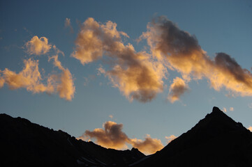A night view of snowy mountains with clouds at sunset. The clouds and sky turn a magnificent golden color as the sun sets.