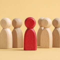 Red Wooden Figurine Standing Out Among Neutral Wooden Figures on Light Yellow Background