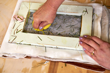 Close-up of hands pressing water out of handmade floral paper with sponge. Final stage of...