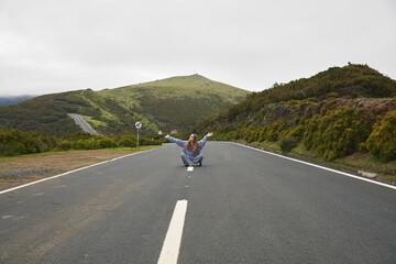 Woman embracing freedom on an empty scenic mountain road under an overcast sky, with arms...