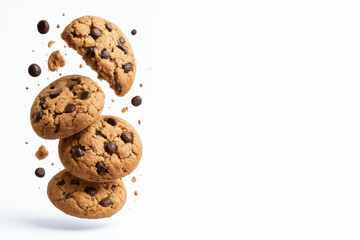 Chocolate chip cookies are stacked and crumbling against white background, with crumbs and chocolate chips scattered around, creating dynamic and appetizing scene with copy space