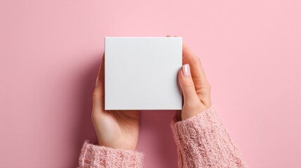 Hands hold a blank white square gift box against a pink background
