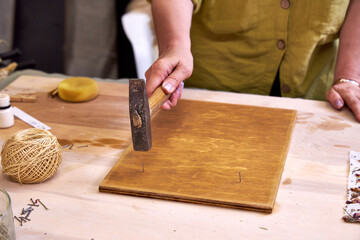 Close-up of woman hammering nails into a stained wood board for handmade decor. Part of...