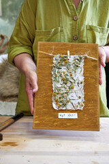 Woman holding finished wall panel made of handmade floral paper on wood. Eco-friendly DIY craft...