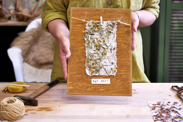 Woman holding finished wall panel made of handmade floral paper on wood. Eco-friendly DIY craft...