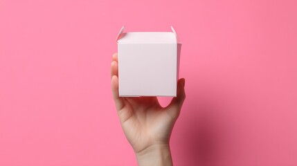 Obraz premium A hand holds a small, blank, white, square box against a pink background