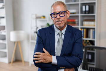 Mid shot of happy middle aged business man or lawyer male ceo standing in office arms crossed....