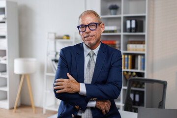 Mid shot of happy middle aged business man or lawyer male ceo standing in office arms crossed....