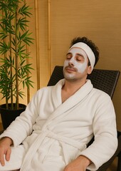Man relaxing in spa chair wearing white robe and facial mask, eyes closed in peaceful wellness environment