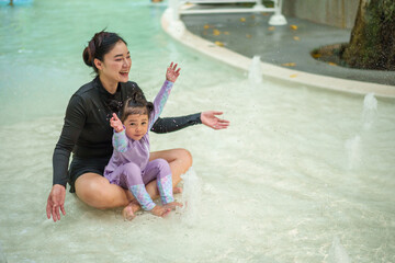 happy mother with toddler girl playing water splashing in swimming pool