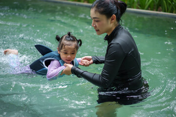 mother teaching toddler girl swimming in pool and wearing life jacket