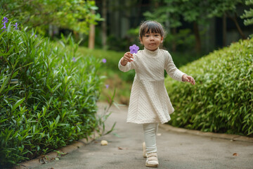 happy toddler girl in white dress with Ruellia simplex or Mexican petunia flower in garden