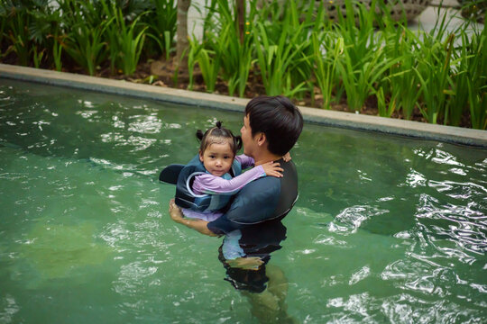 father with toddler girl in life jacket playing in swimming pool